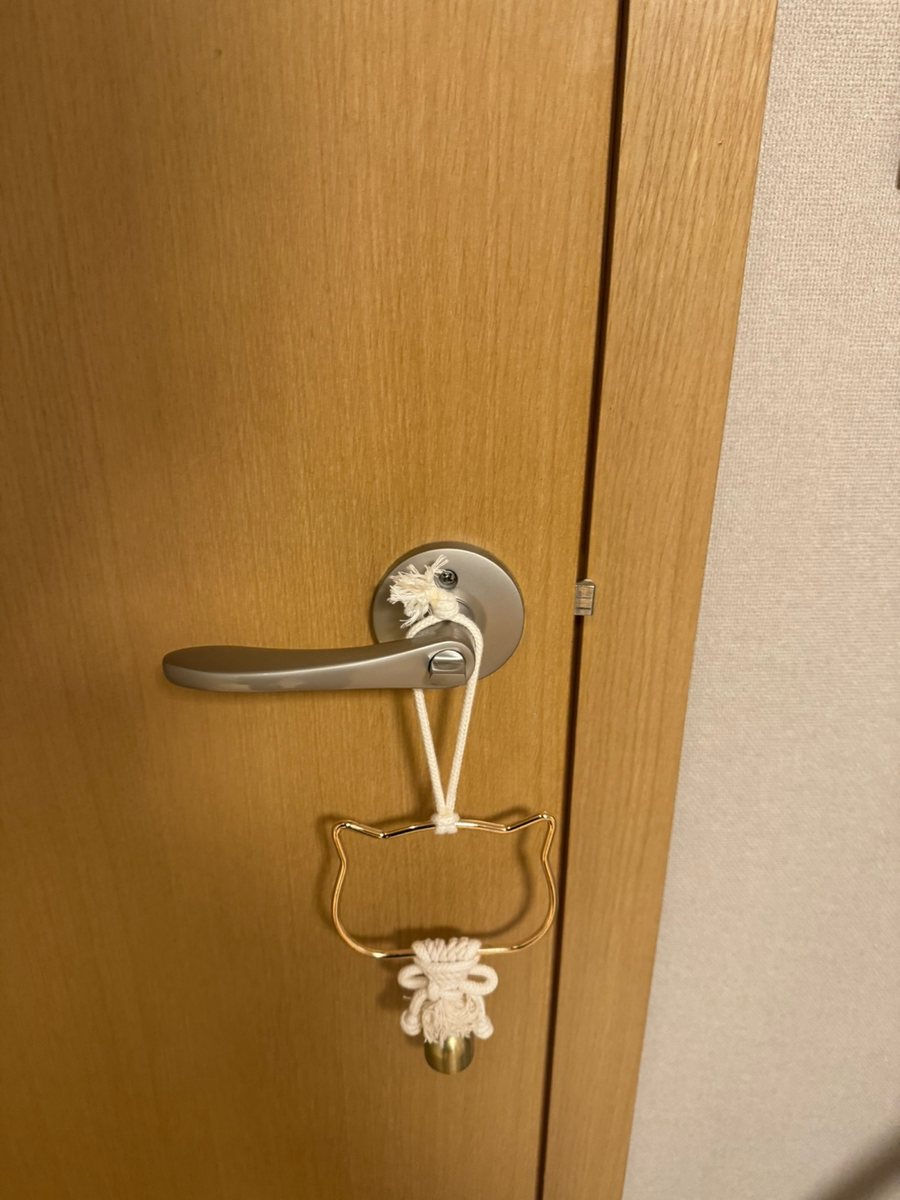 오정구 오정동 출장 — 밝은 갈색 나무 문에 단 은색 레버 손잡이와 걸려 있는 고양이 얼굴 모양 고리 장식